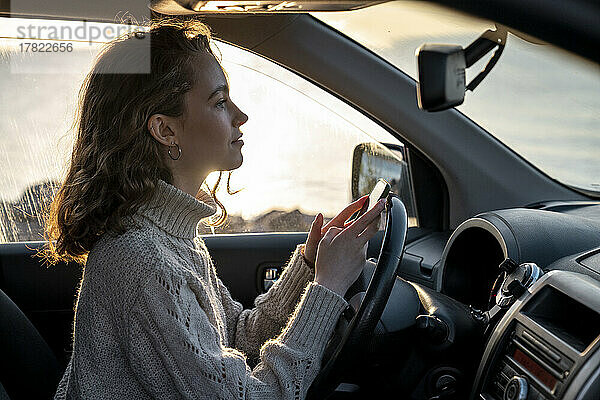 Lächelnde junge Frau mit Smartphone sitzt im Auto