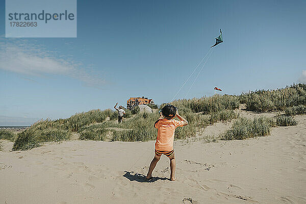 Junge lässt Drachen mit Vater an sonnigem Tag am Strand steigen