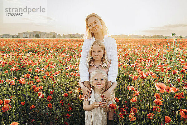 Lächelnde Mutter mit Töchtern  die im Mohnfeld stehen