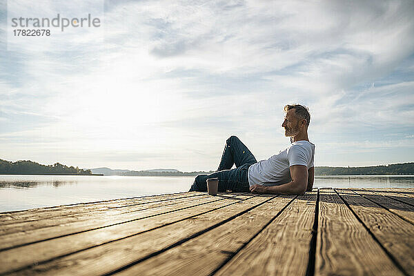 Reifer Mann entspannt sich bei einer Einweg-Kaffeetasse am Pier am See