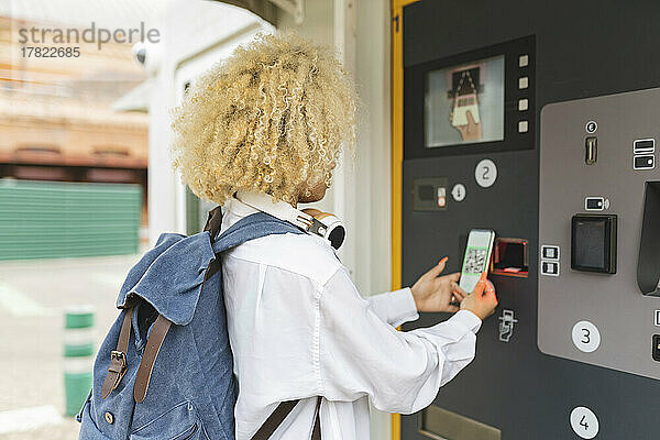 Frau benutzt Ticketautomaten und scannt QR-Code über Smartphone