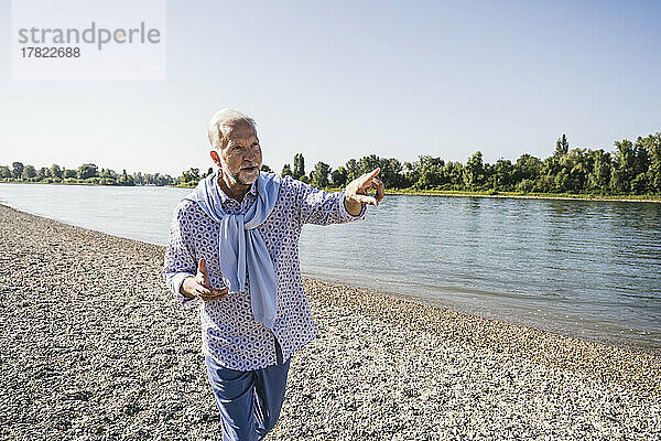 Älterer Mann gestikuliert und geht am Flussufer