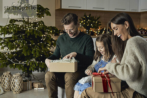 Glückliche Eltern mit Tochter öffnen Weihnachtsgeschenk im Wohnzimmer