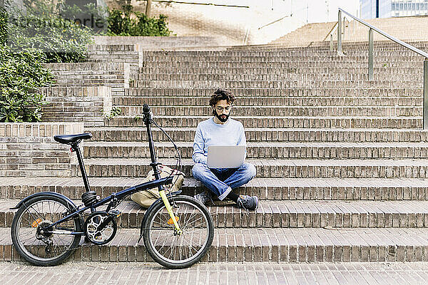 Freiberufler sitzt mit Laptop auf Stufen neben Fahrrad