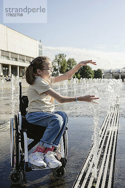 Mädchen im Rollstuhl spielt an sonnigem Tag mit Brunnen