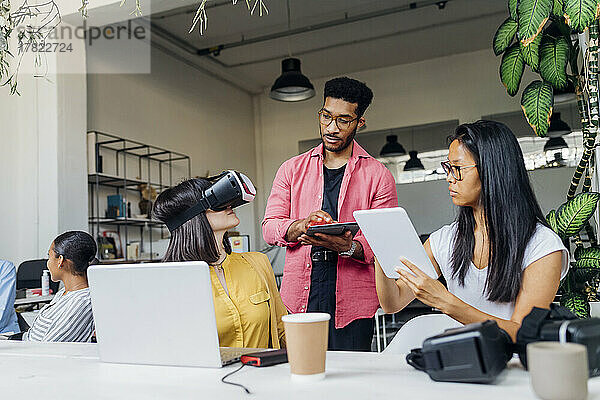 Geschäftskollegen halten Tablet-PCs in der Hand einer Geschäftsfrau mit VR-Brille im Büro