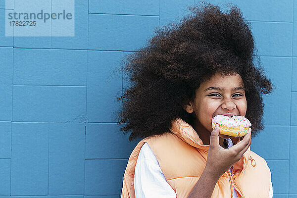 Hungriges Mädchen isst Donut und steht vor der blauen Wand