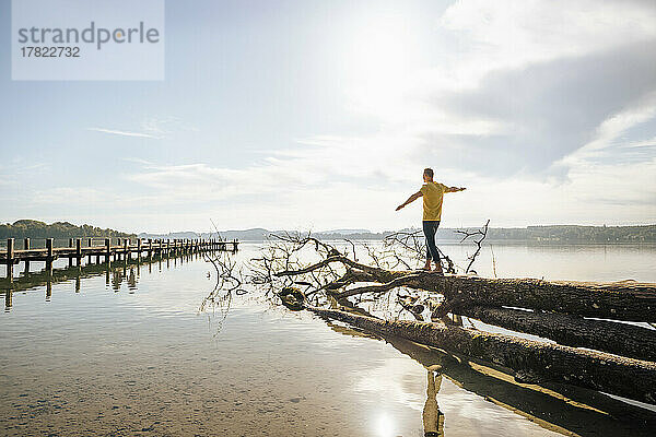 Mann balanciert auf umgestürztem Baumstamm am See