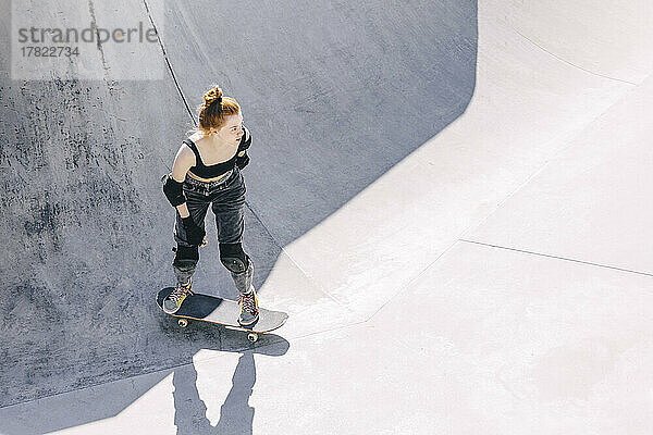 Nachdenklicher Teenager steht an sonnigem Tag auf dem Skateboard