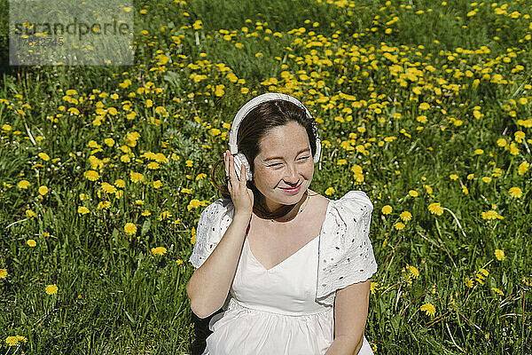 Lächelnde Frau  die inmitten blühender Pflanzen über Kopfhörer Musik hört