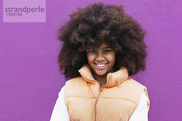 Lächelndes Mädchen mit Afro-Frisur vor violettem Hintergrund