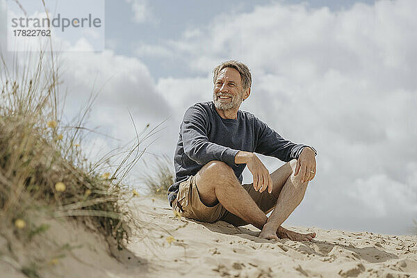 Happy mature man sitting on sand