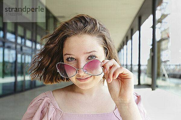 Lächelndes Teenager-Mädchen mit braunen Haaren und rosa Brille