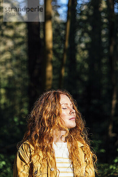 Junge Frau mit geschlossenen Augen genießt das Sonnenlicht im Wald