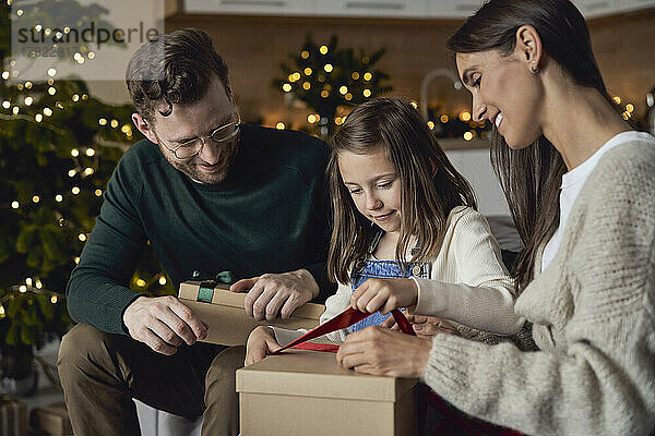 Mädchen öffnet Weihnachtsgeschenk und sitzt mit den Eltern zu Hause