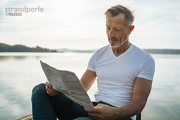 Mature man reading newspaper sitting by lake