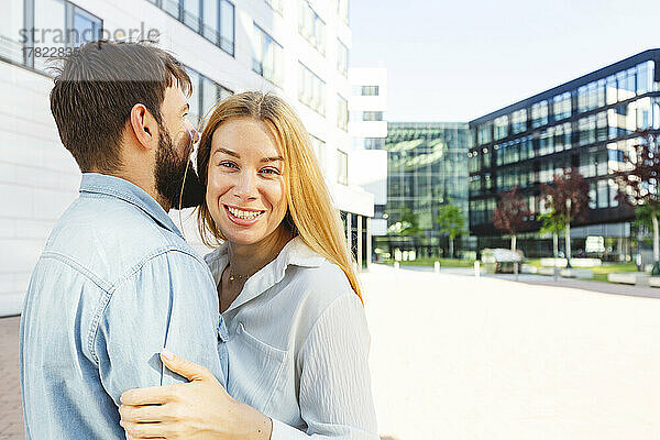 Fröhliche blonde Frau mit Freund steht vor dem Gebäude