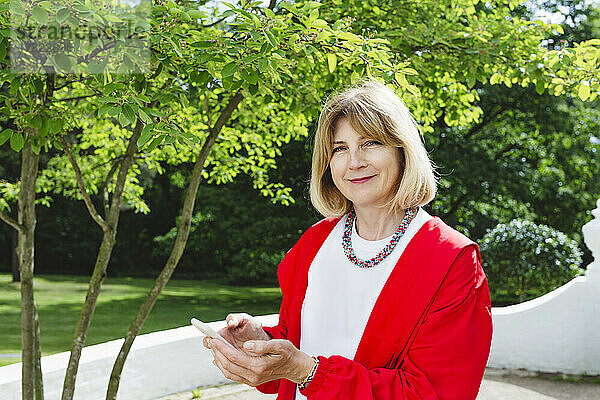 Lächelnde Frau hält Smartphone im Garten
