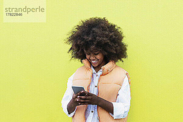 Glückliches Mädchen  das Smartphone vor gelbem Hintergrund benutzt