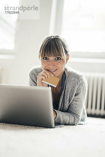 Lächelnde Frau mit Kreditkarte und Laptop zu Hause