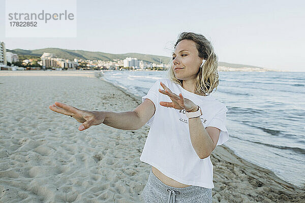 Glückliche Frau mit kabellosen In-Ear-Kopfhörern tanzt am Strand