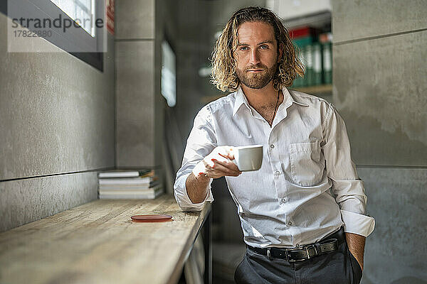 Geschäftsmann steht im Büro mit der Hand in der Tasche und trinkt Kaffee