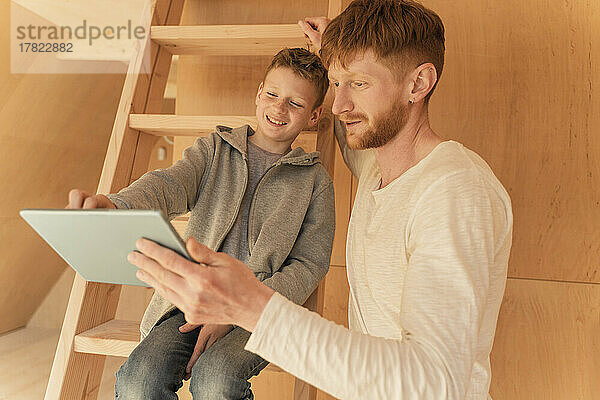 Vater und Sohn nutzen Tablet-PC  um die Inneneinrichtung eines Öko-Holzhauses zu gestalten