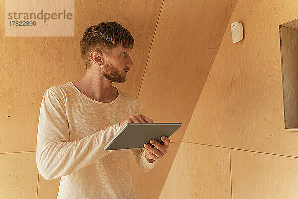 Mann richtet eine Smart-Home-Einheit mit digitalem Tablet in einem Öko-Haus ein