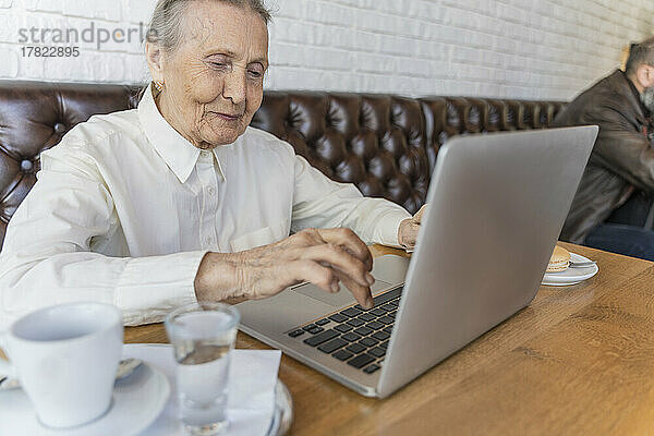 Lächelnde ältere Frau benutzt Laptop im Café