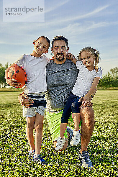 Glücklicher Mann mit Tochter und Sohn  die Rugbyball auf dem Sportplatz halten