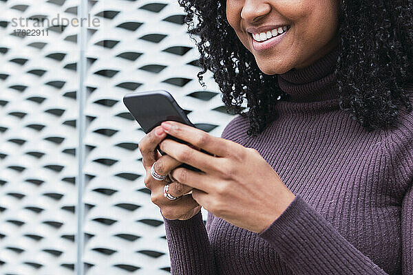 Glückliche Frau  die mit ihrem Mobiltelefon vor der Wand im Internet surft