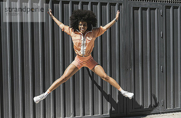 Fröhliche Afro-Sportlerin springt vor schwarzer Wand