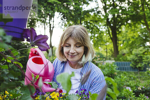Lächelnde Frau  die Gartenblumen gießt