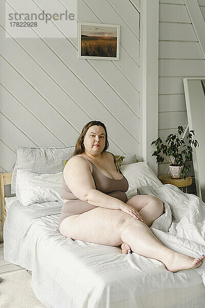 Woman wearing bikini sitting on bed at home