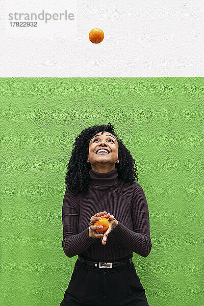 Glückliche Frau wirft Orange vor grüne Wand