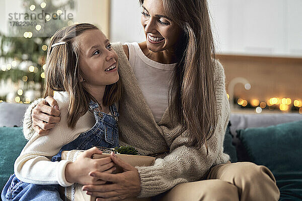 Glückliche Mutter umarmt ihre Tochter  die im Wohnzimmer sitzt