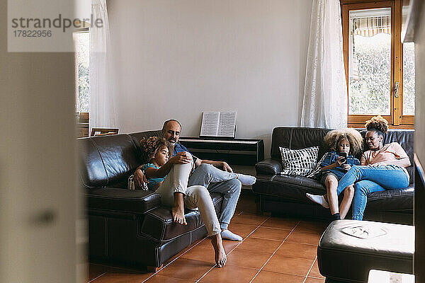 Eltern schauen sich Kinder an  die Mobiltelefone benutzen  die auf dem Sofa im Wohnzimmer sitzen