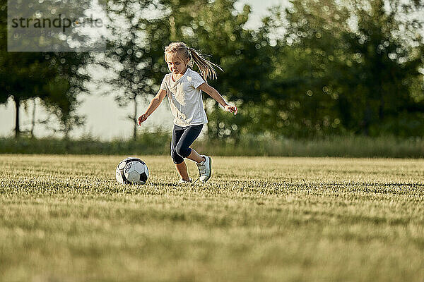 Girl playing soccer at sports field on sunny day