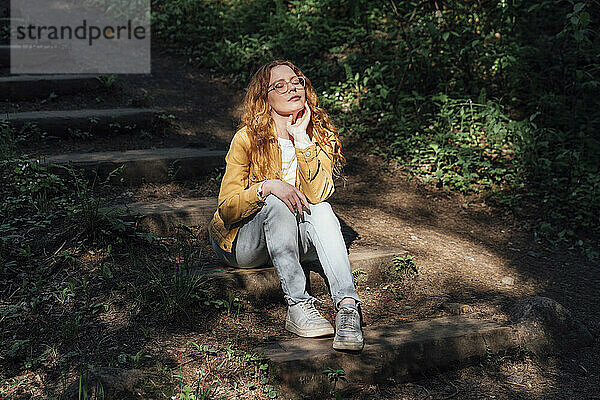 Junge Frau mit geschlossenen Augen genießt das Sonnenlicht im Wald