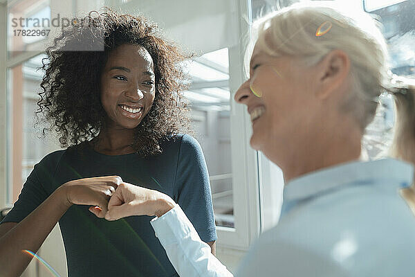 Lächelnde Geschäftsfrau gibt ihrem Kollegen im Büro einen Faustschlag
