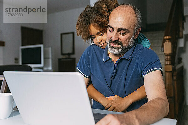 Mädchen umarmt Vater mit Laptop und arbeitet von zu Hause aus