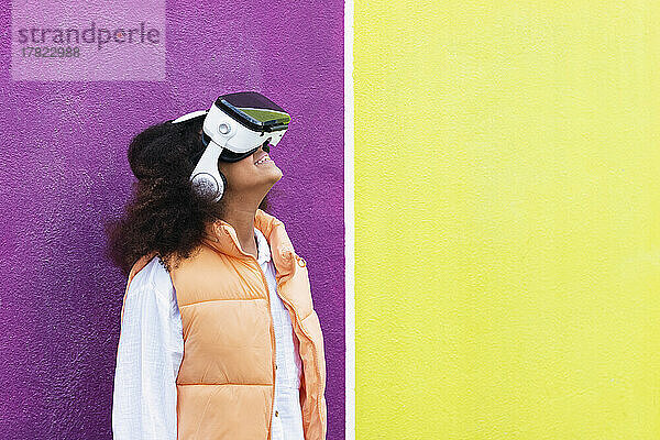 Mädchen mit Virtual-Reality-Simulator steht vor gelber und violetter Wand