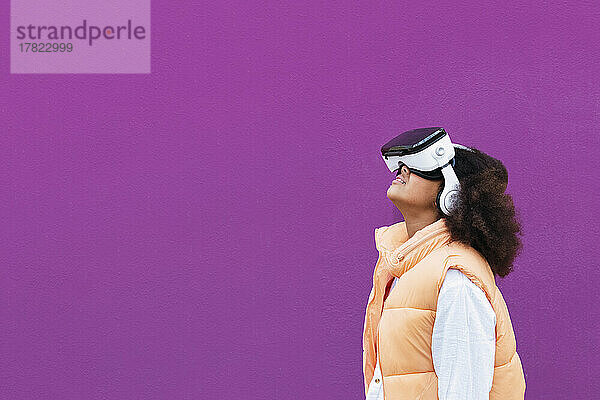 Mädchen mit Virtual-Reality-Simulator steht vor violettem Hintergrund