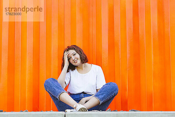 Lächelndes Teenager-Mädchen sitzt vor einem orangefarbenen Frachtcontainer