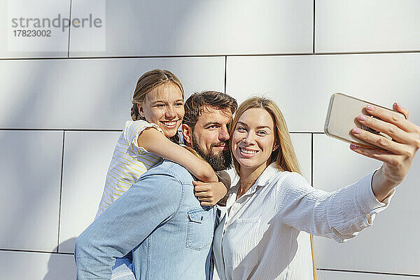 Glückliche Frau macht ein Selfie mit der Familie per Smartphone vor der Wand