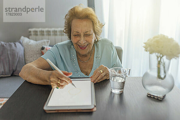 Glückliche ältere Frau mit Tablet-PC am Tisch sitzend