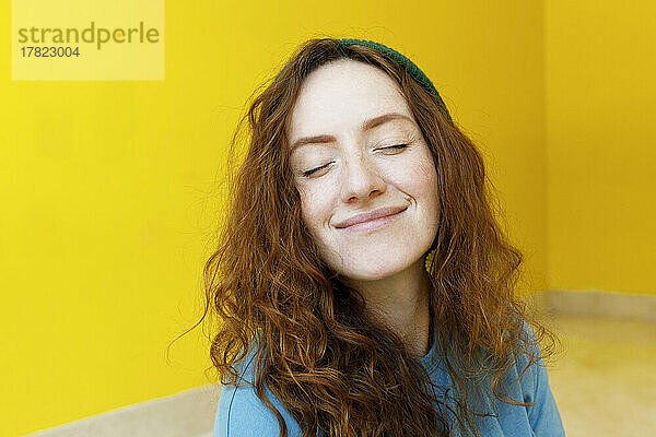 Lächelnde Frau mit geschlossenen Augen vor gelber Wand