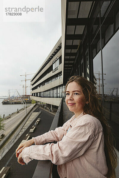 Lächelnde junge Frau steht auf dem Balkon am Hafen