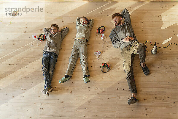 Father and kids have rest  lying after sanding the floor in an eco house. Top view  time together