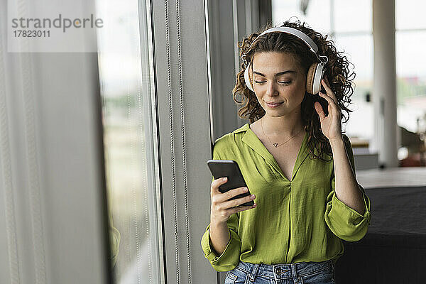 Geschäftsfrau trägt Kopfhörer und hört im Büro Musik über ihr Smartphone